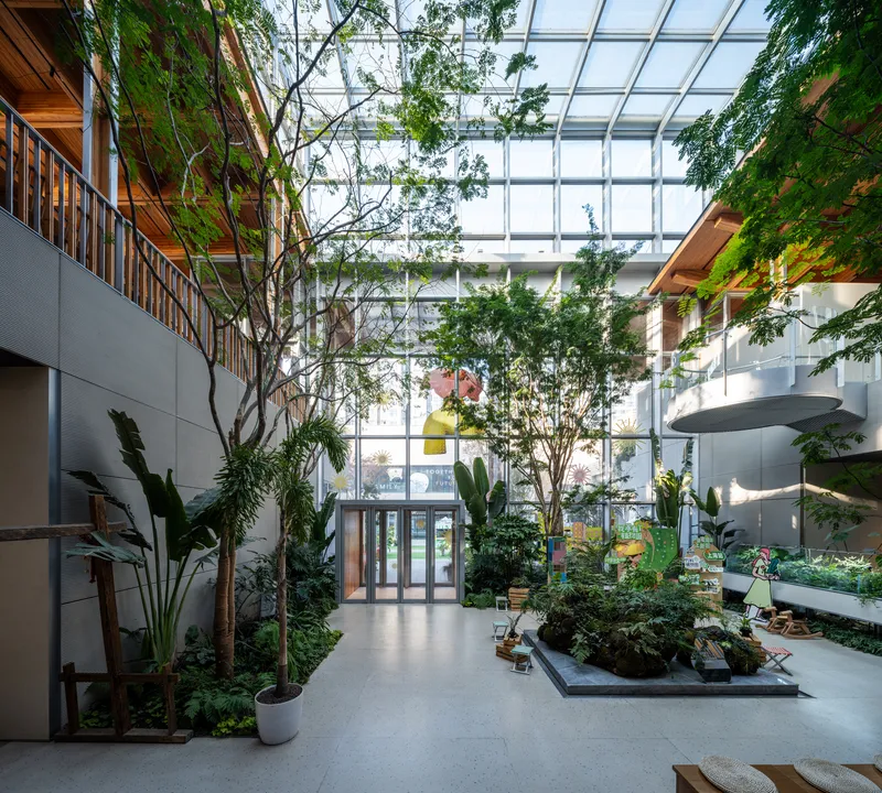 Interior courtyard atrium with full-height glass skylight, mature trees, and planted beds on polished floor