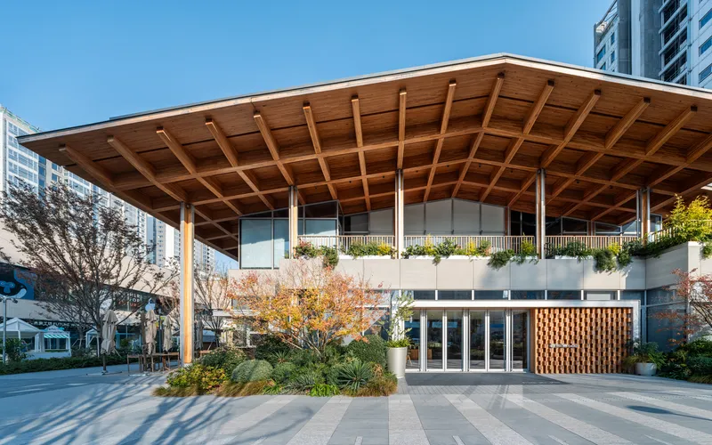 Front entrance with timber-cofferred canopy roof, planted courtyard and high-rise towers in the background