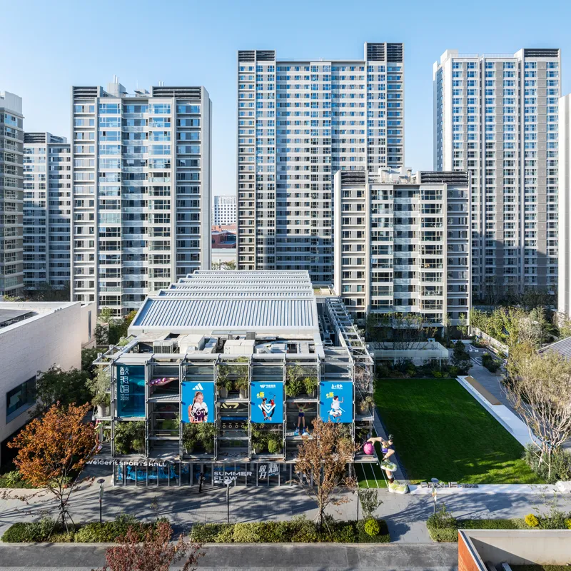 Aerial view of the low-rise pavilion with ribbed roof surrounded by residential towers and green plaza