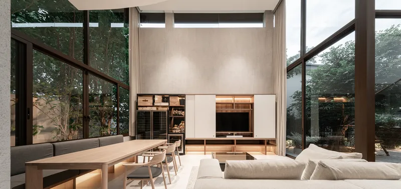 Double-height living space with media wall, dining table, and full-height windows at dusk
