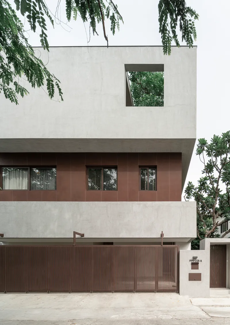 Street facade with stacked concrete and copper-clad volumes framed by overhanging tree branches