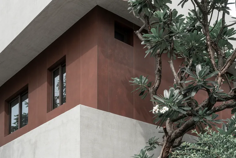 Corner detail showing the copper panel cladding meeting white stucco wall beside a flowering frangipani tree