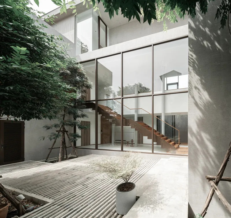 Interior courtyard with ribbed concrete ground surface and glazed stairwell framed by planted trees casting shadows