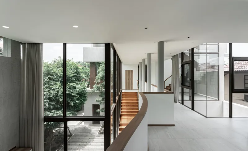 Upper floor landing with curved timber staircase overlooking courtyard through floor-to-ceiling glass walls