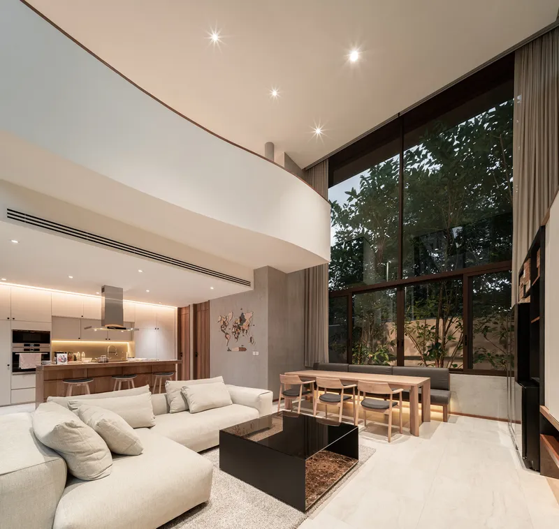 Double-height living space with open kitchen and glazed wall overlooking garden at dusk