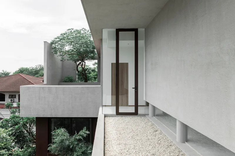 Upper level terrace with gravel flooring and glazed door beneath an angled concrete overhang