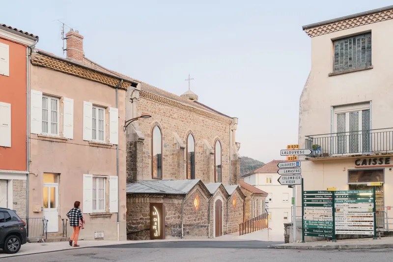 Street view of renovated stone church entrance nestled between residential buildings with person crossing