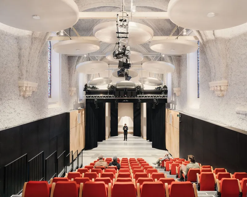 Interior auditorium with red seating, white disc ceiling panels, stained glass windows and theatrical rigging
