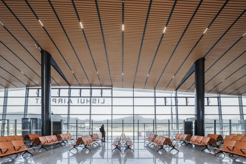 Departure gate seating area with wood-slat ceiling and floor-to-ceiling glazing overlooking the airfield