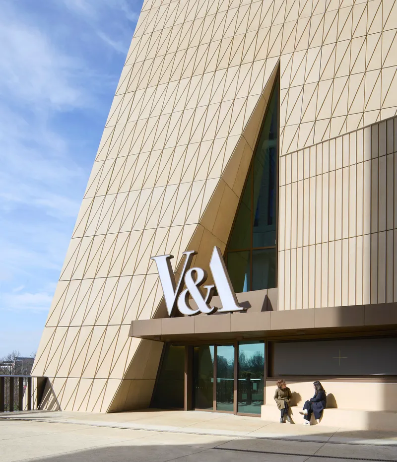 Angled facade with triangular geometric panel cladding and cantilevered entrance canopy under a clear blue sky