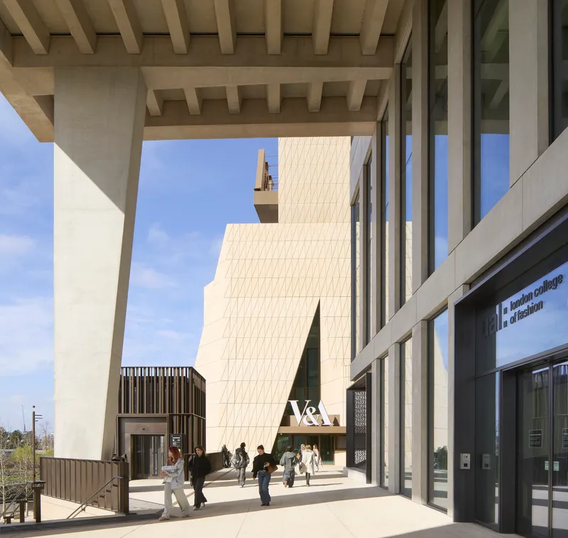 Covered colonnade with exposed concrete beams framing views of the paneled facade and visitors passing through