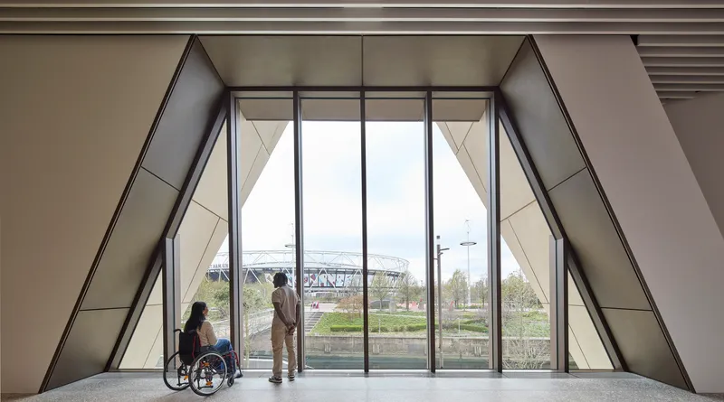 Interior gallery space with floor-to-ceiling triangular glazing overlooking the landscape and two visitors conversing