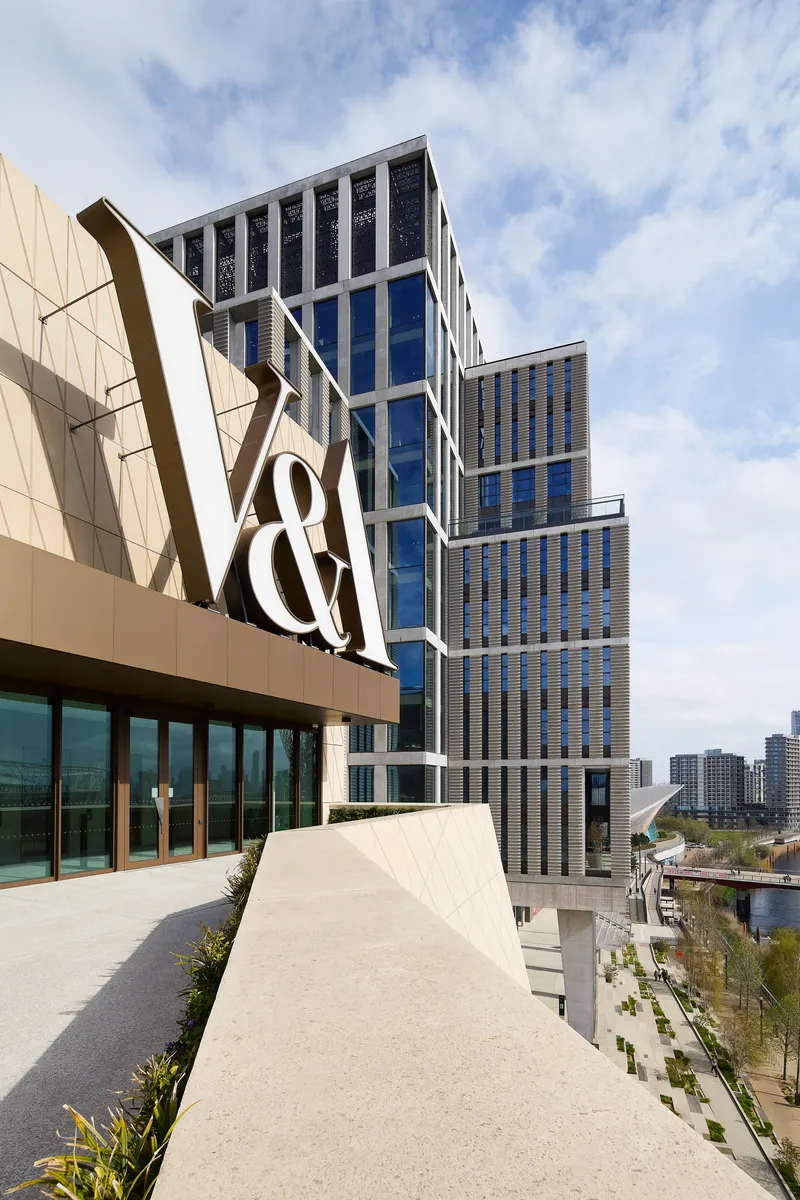 Rooftop terrace with geometric paving and angled facade forms rising beside a stepped glass tower under cloudy skies