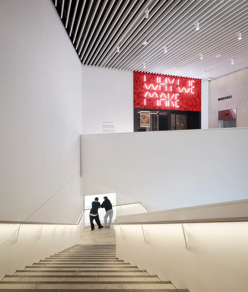 Wide staircase with integrated lighting and two visitors ascending toward the red neon installation above