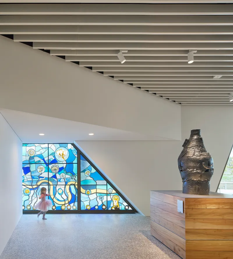 Stained glass window fills triangular wall beside timber reception desk and terrazzo floor