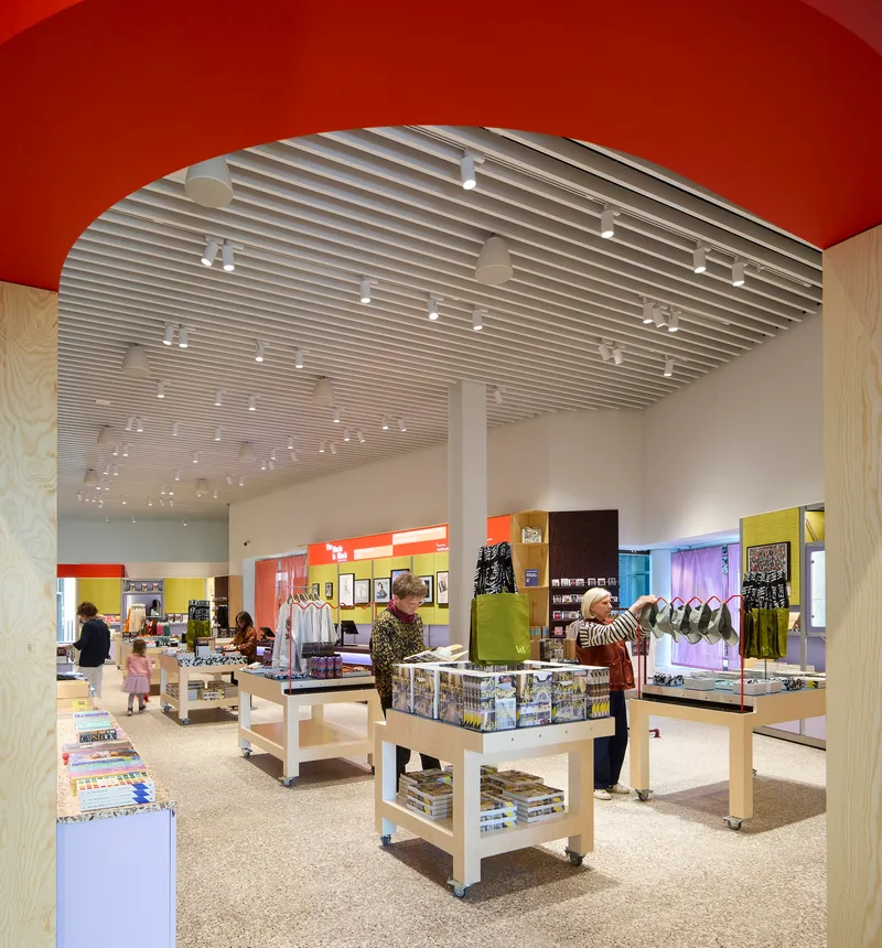 Museum shop with white display tables under archway framed by red ceiling plane