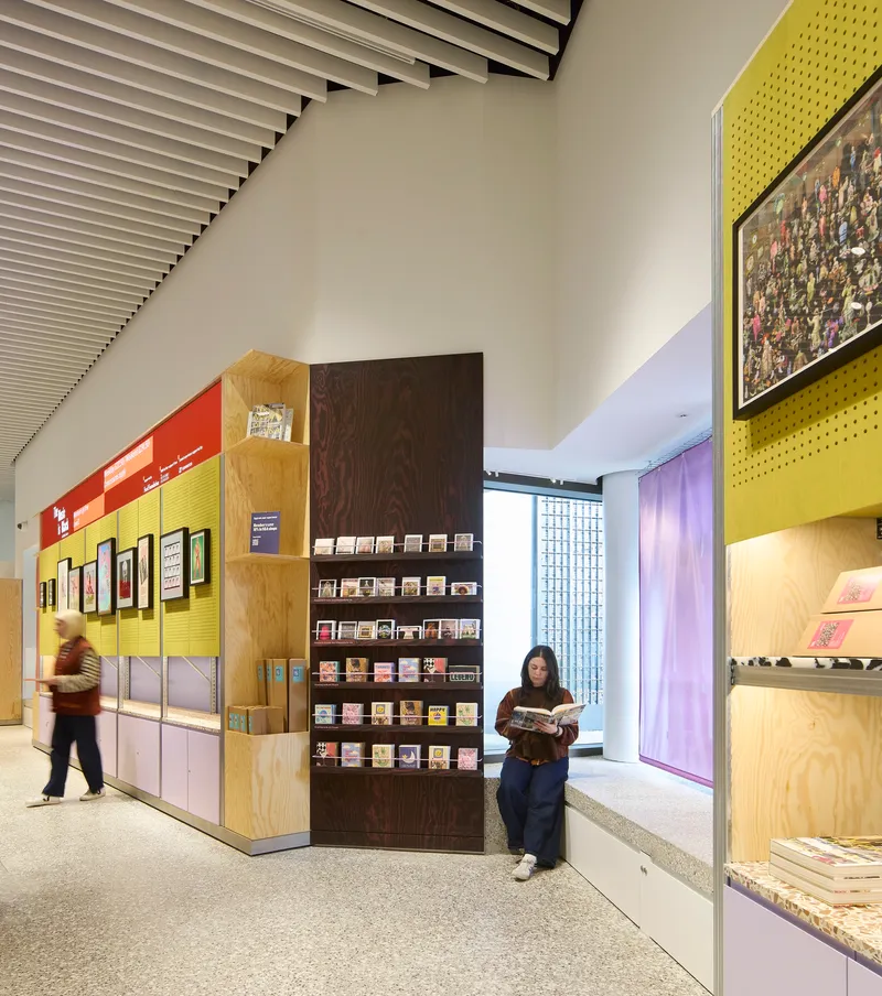 Visitor reading beside freestanding display wall with yellow pegboard and plywood shelving