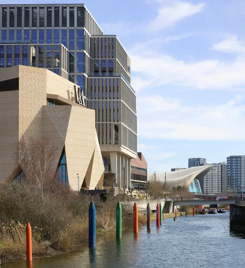 Canal waterway with colorful timber pilings and the angular tiled volume set against stepped residential towers