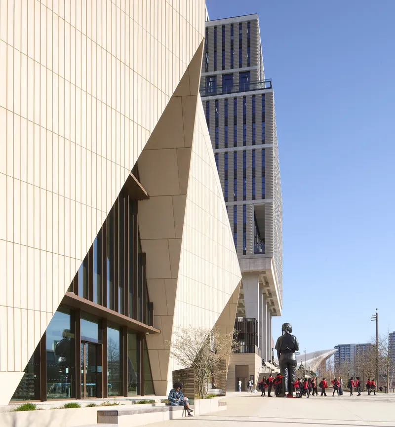 Public plaza with bronze sculpture and visitors in front of the angular entrance volume