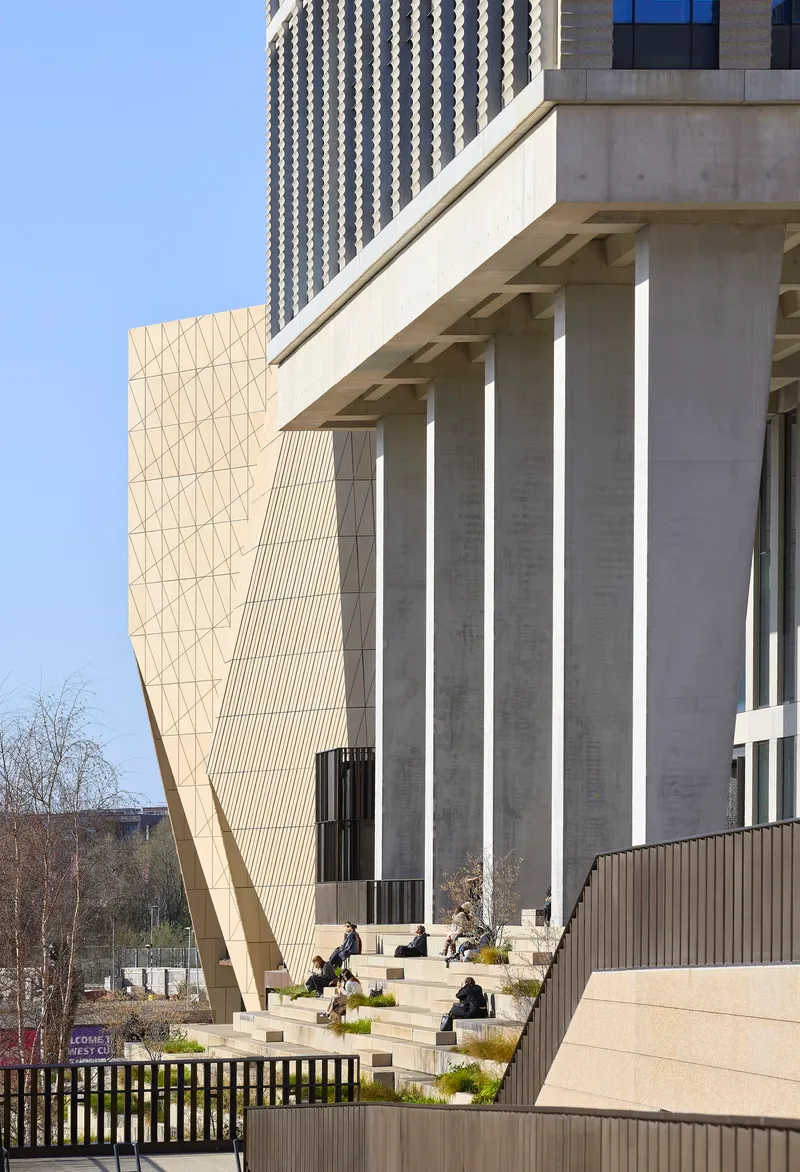 Concrete colonnade at ground level with visitors seated on planted terraces beside the sculptural facade