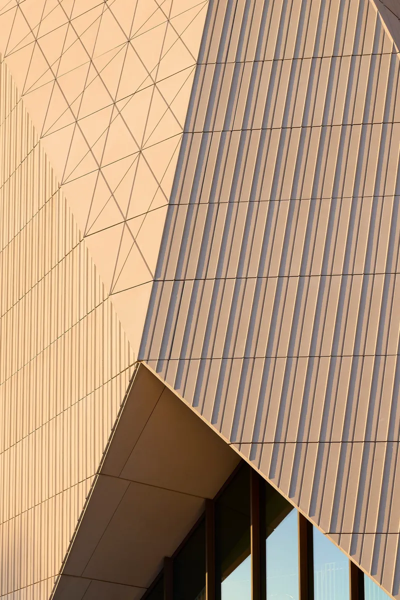 Facade detail showing triangular and vertical panel patterns meeting at an angular entrance canopy