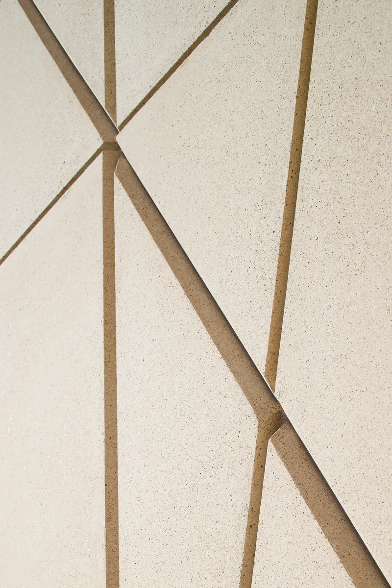 Detail of pale facade surface with brass or bronze inlay forming triangular geometric pattern