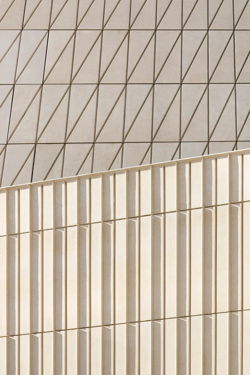 Two facade surfaces with contrasting patterns of diagonal grooves and vertical flutes meeting at a corner