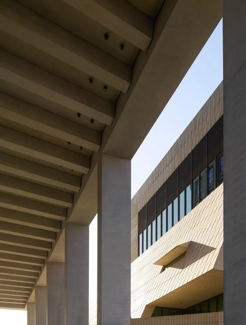 Courtyard view framed by ribbed concrete canopy and facade with angular protruding window opening