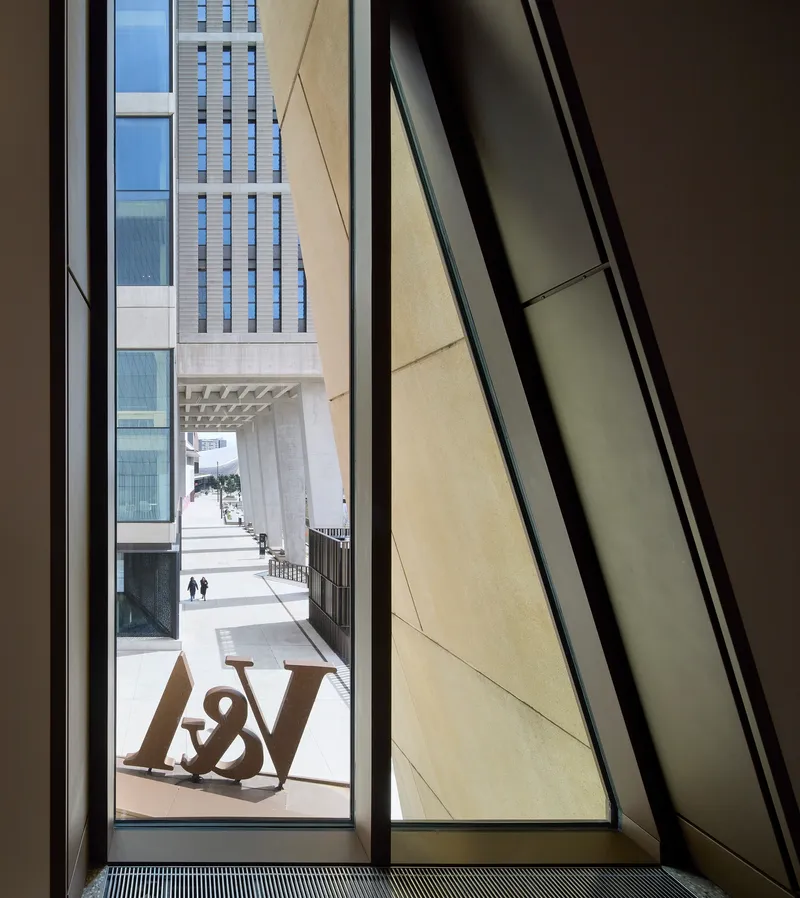 Angled window framing a view of the courtyard with chequered tower facade and pedestrians in bright daylight