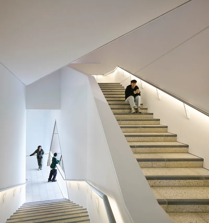 Multi-level stairwell with terrazzo treads and integrated handrail lighting as visitors descend and pause