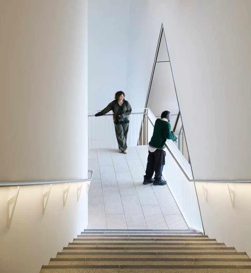 Upper landing with triangular metal railing overlooking the stairwell below where two visitors stand