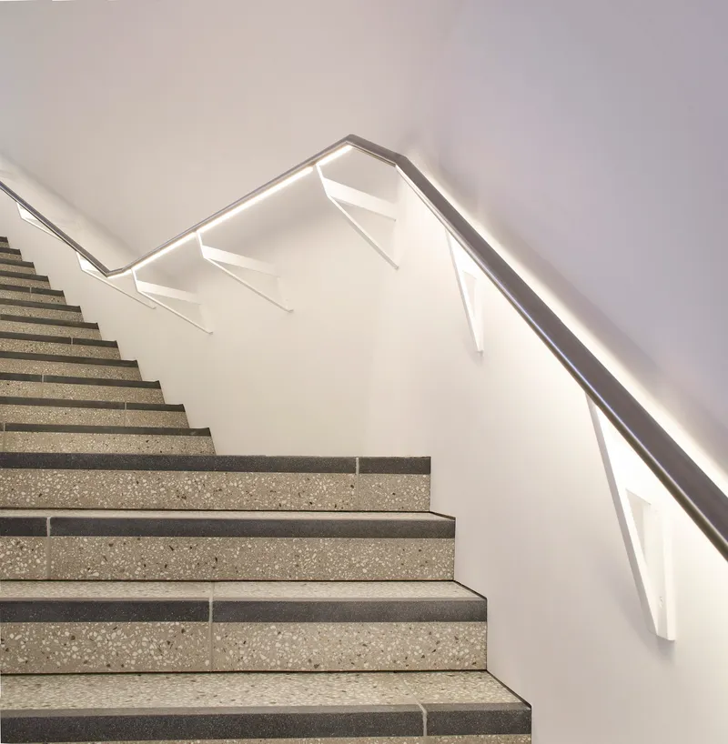Close-up of the folded metal handrail with integrated LED strip along the terrazzo stair flights