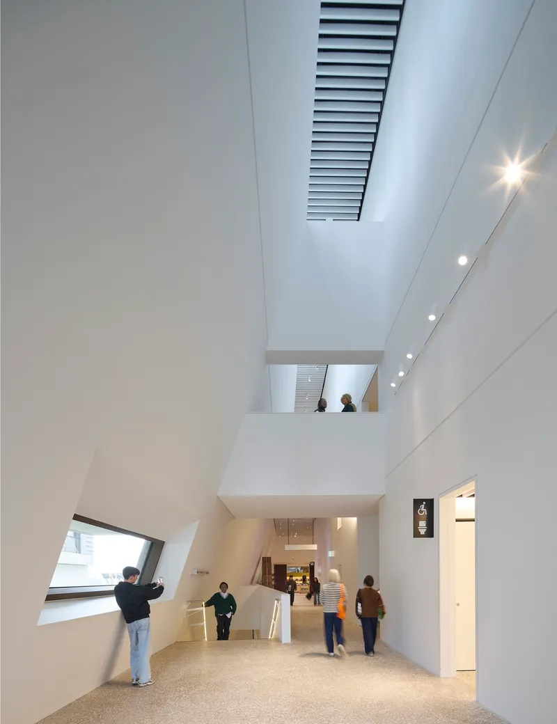 Double-height atrium with angled window, internal balcony and visitors moving through the terrazzo-floored circulation space