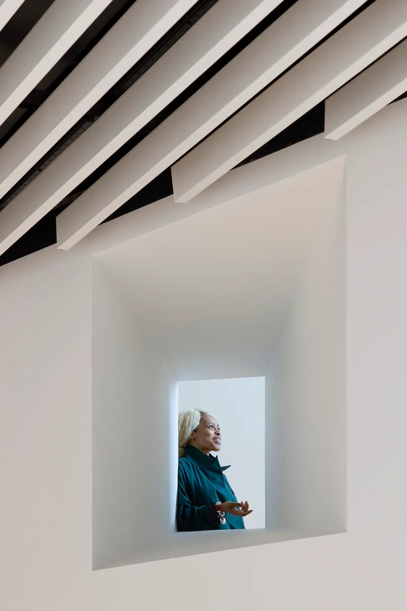 Deep framed window opening with a visitor looking outward beneath angled ceiling louvers