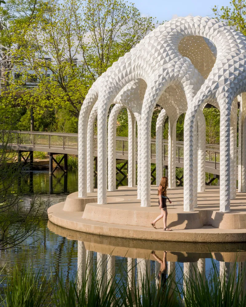 White patterned columns supporting domed canopy over circular platform with person walking in afternoon light