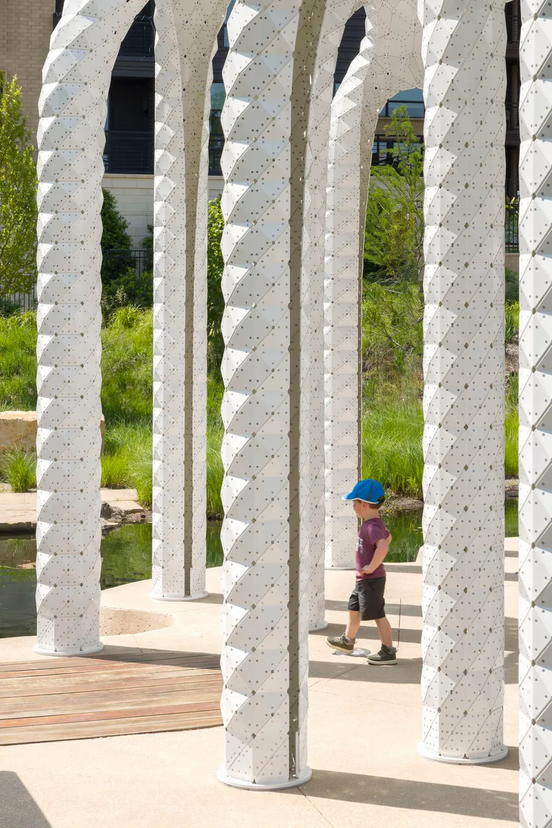 Close view through textured white columns with child in blue cap walking on timber decking