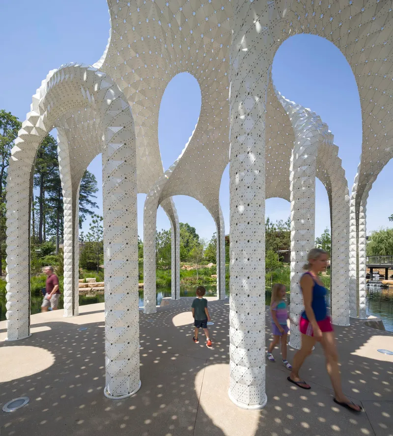 Interior view through perforated columns casting dappled shadows as visitors walk through the pavilion