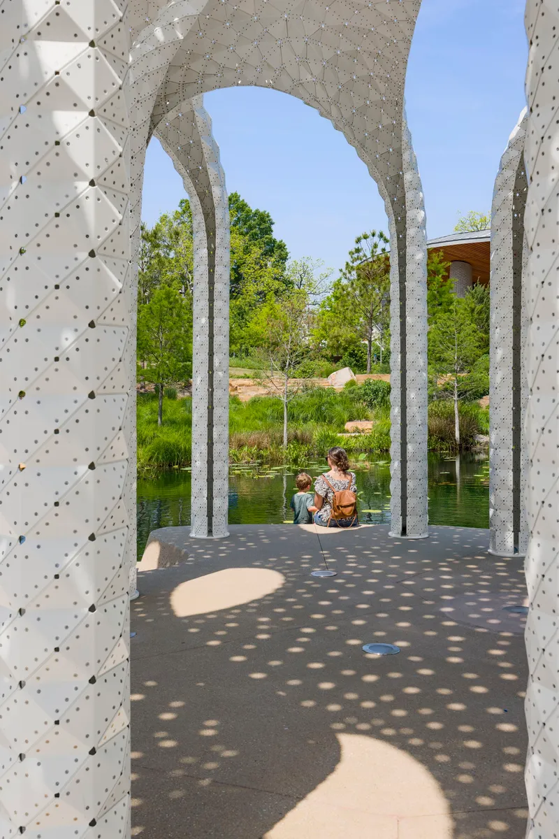 View through arched openings with visitors seated on the pavilion floor overlooking the pond