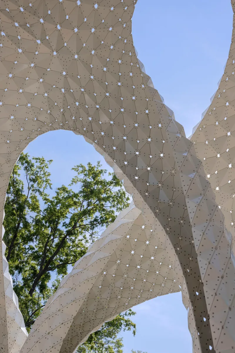 Close-up of the perforated shell structure showing the tiled surface pattern with trees visible beyond