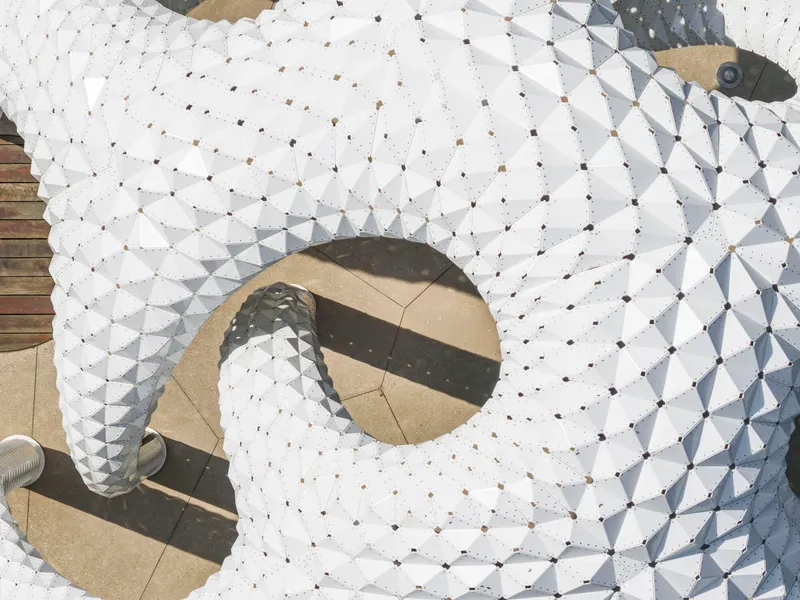 Aerial view of white faceted panels forming circular openings with people casting shadows below
