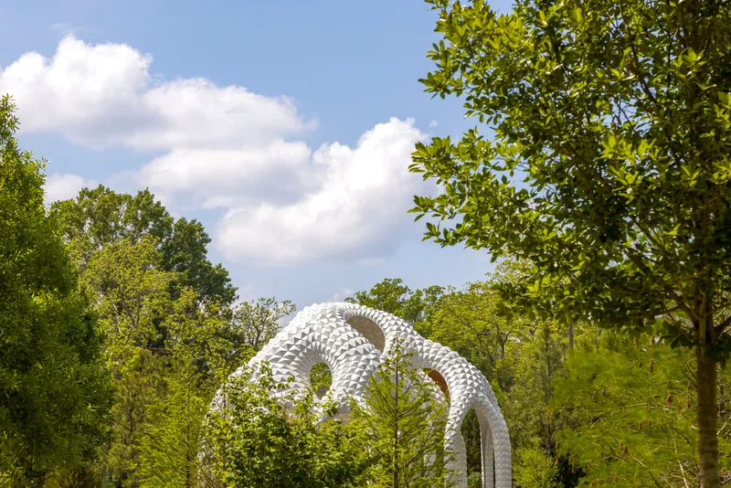 White sculptural loops rising above tree canopy on a partly cloudy summer day
