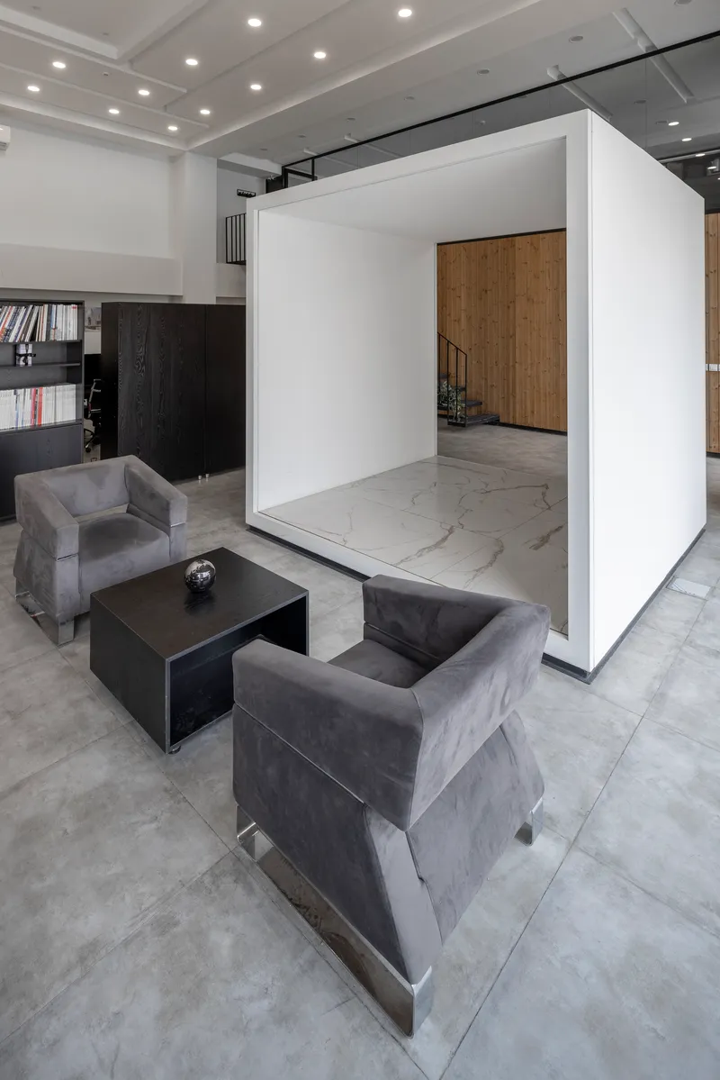 Freestanding white box volume with marble floor framing a view to timber-clad staircase beyond