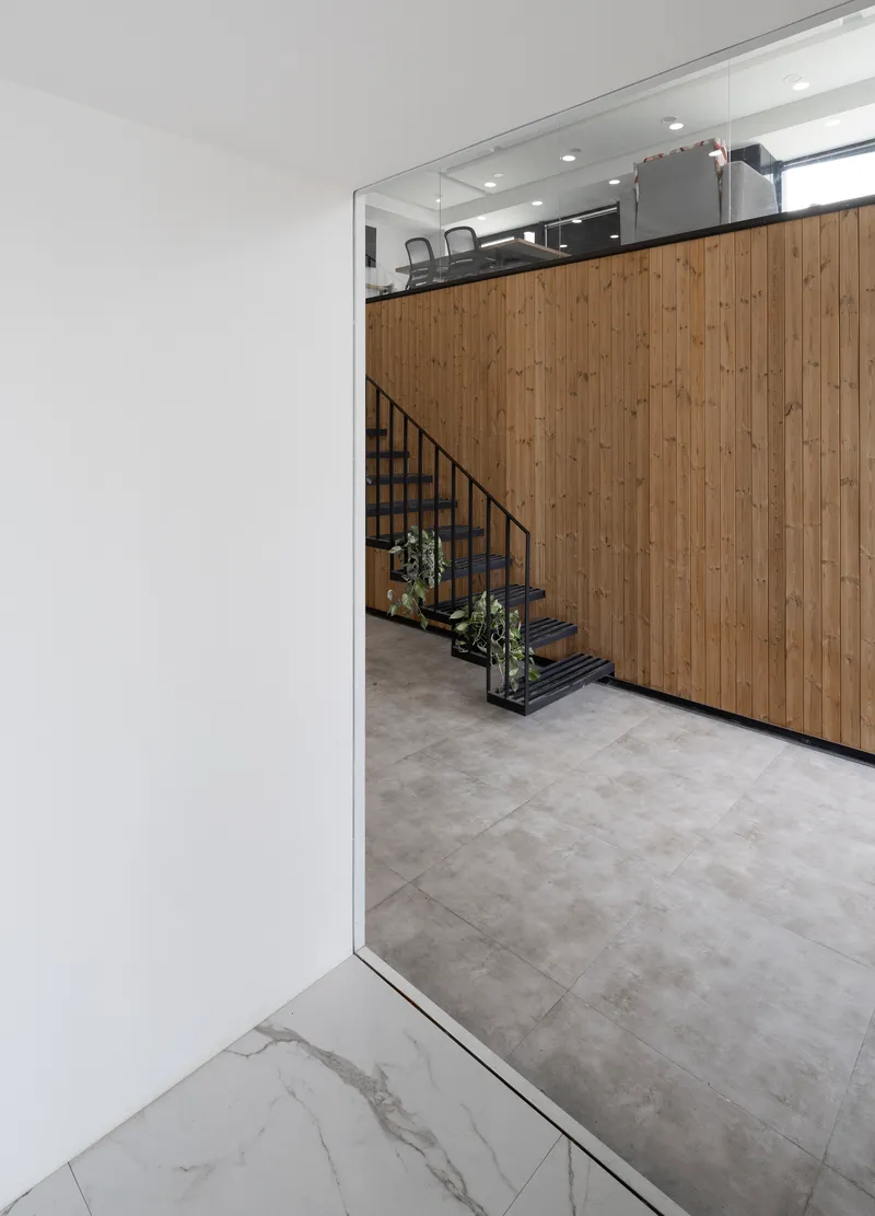 Timber-clad wall with integrated staircase viewed through a doorway from the marble-floored entrance