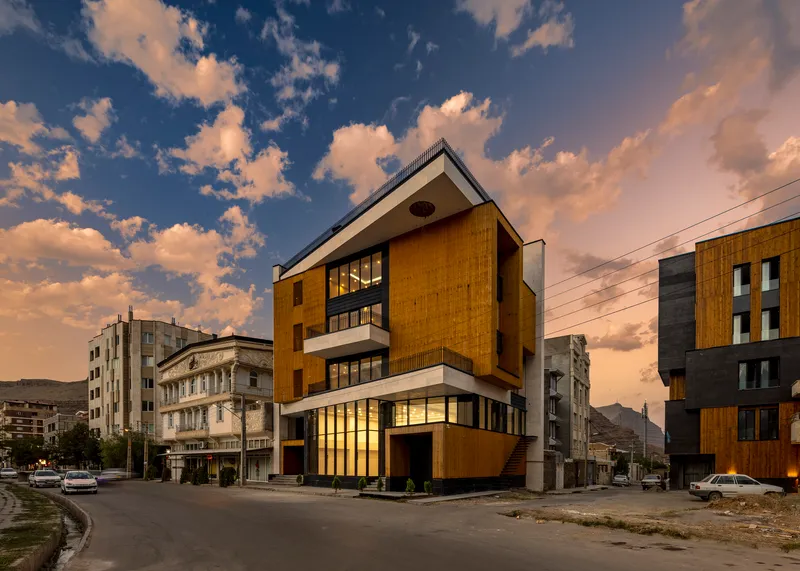 Corner facade with timber and glazed panels at dusk beneath a cloudy blue sky