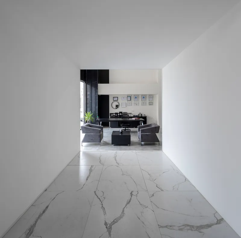 White corridor with veined marble tile floor leading to a seating area with framed artworks