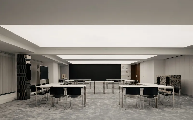 Meeting space arranged with white tables in clusters beneath linear ceiling skylights and patterned grey carpet