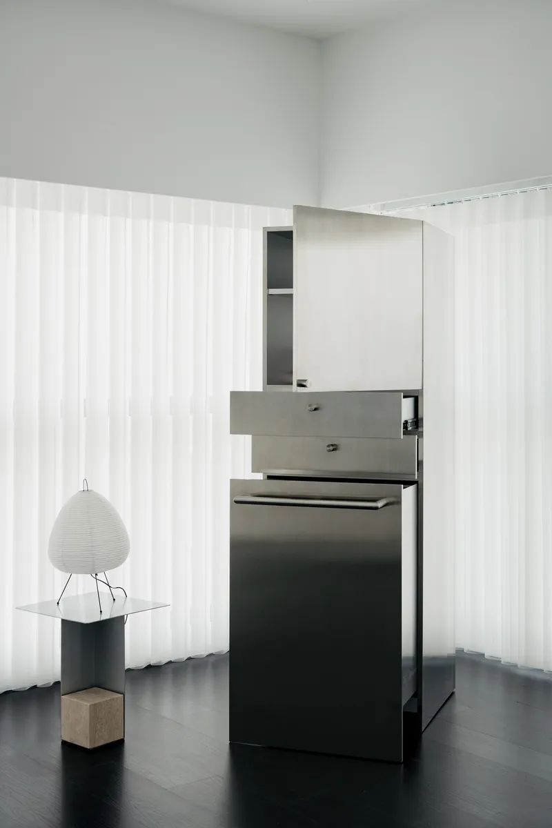 Freestanding kitchen counter with grey drawers and black cabinetry against translucent corrugated wall panels