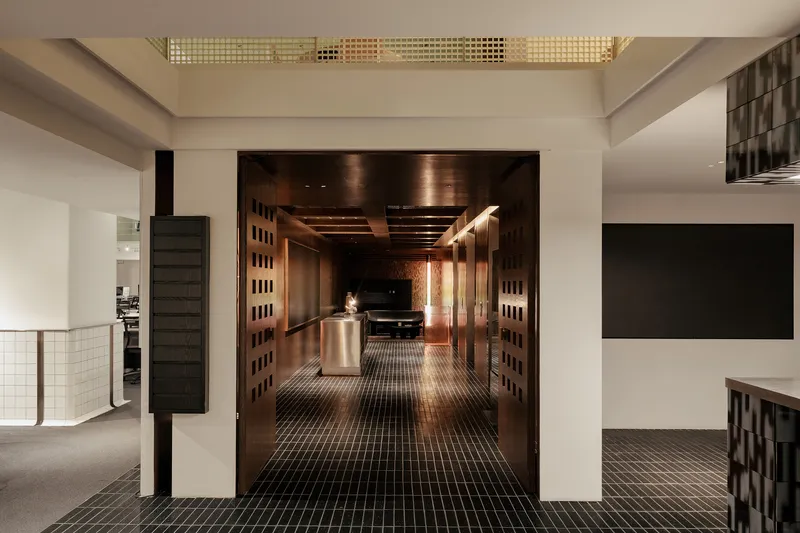 View through double doors into a timber-lined corridor from a white reception area with gridded skylights