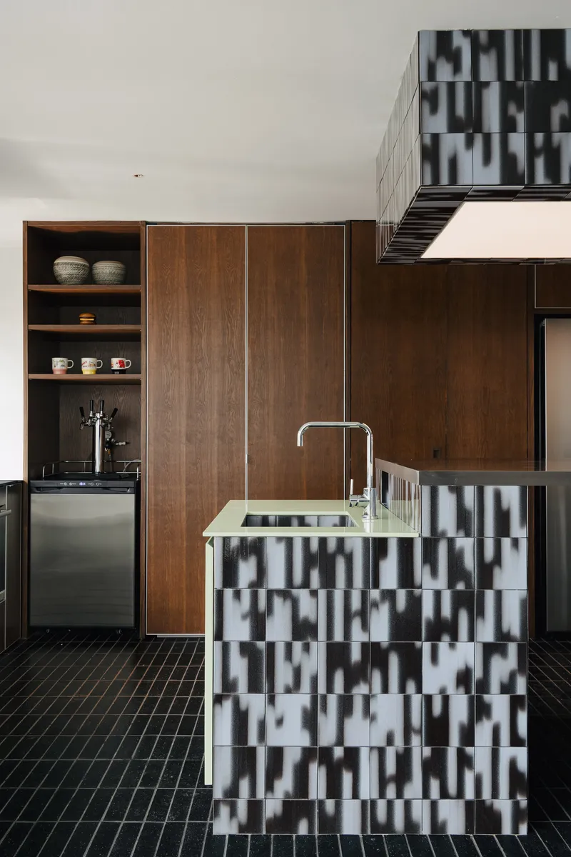 Kitchen island clad in black and white chequered tiles with walnut cabinetry and open shelving