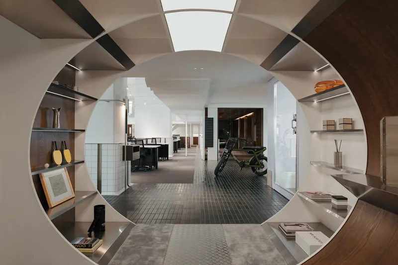 View through a circular portal framed by timber shelving into an interior space with grey mosaic tile flooring